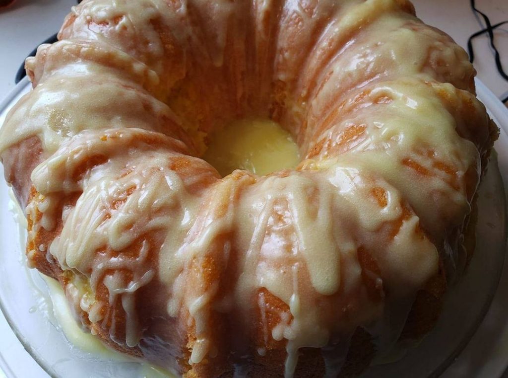 Lemon cake with cream cheese glaze and fresh lemon zest on a white platter.