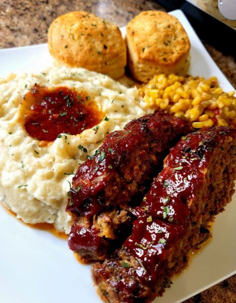 A close-up photograph of a delicious and moist meatloaf topped with ketchup and herbs