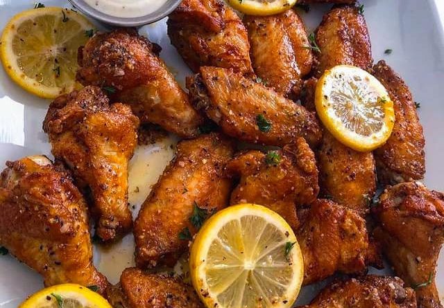 Crispy lemon pepper chicken wings on a white plate garnished with parsley and lemon wedges