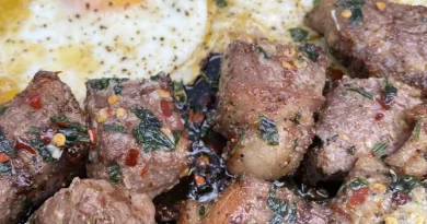 Ribeye steak bites covered in garlic-infused butter, served with sunny-side-up eggs on a plate.