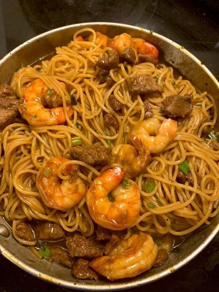 Close-up of a forkful of shrimp and steak teriyaki noodles, with pink shrimp, tender slices of sirloin steak, and thin noodles coated in a flavorful teriyaki sauce.