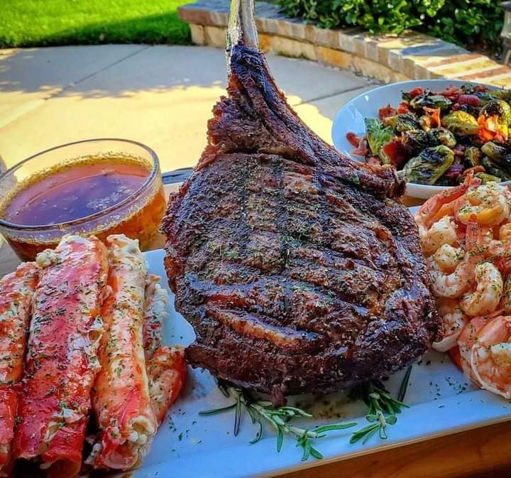 A beautifully plated Tomahawk steak, king crab, shrimp and brussel sprouts on a white plate