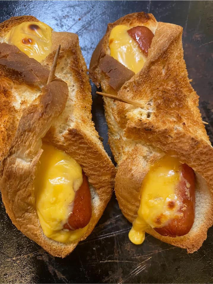 A plate of toasted hot dog roll-ups with toppings of cheese, bacon, ketchup, mustard, and lettuce