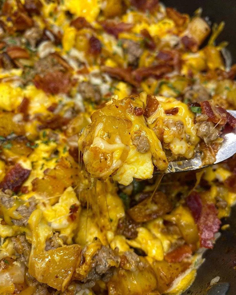 A skillet of one pot breakfast with potatoes, sausage, scrambled eggs, and bacon, ready to be served