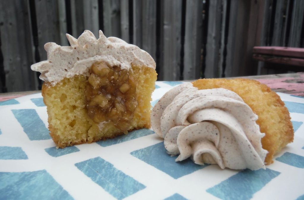Photo of a tray of perfectly frosted Apple Pie Cupcakes, showcasing the spiced apple filling visible through a cut-out section on top.