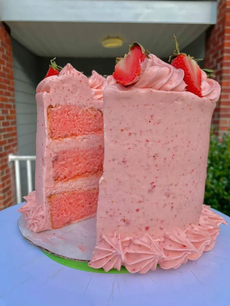 Homemade strawberry cake topped with strawberry buttercream frosting on a white cake stand