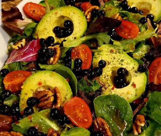 Blueberry Avocado Salad - Fresh spring mix greens, creamy avocados, plump blueberries, toasted pecans, grape tomatoes, and crumbled feta cheese in a bowl.