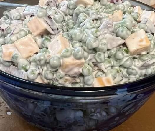 Classic Pea Salad: A bowl filled with vibrant green peas, crispy bacon, diced red onion, and cubed cheddar cheese, coated in a creamy dressing.