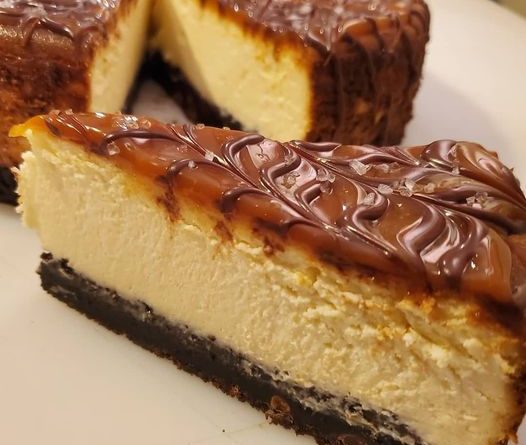 Salted Caramel Brownie Cheesecake on a cake stand, showcasing layers of fudgy brownie, creamy cheesecake, and a drizzle of salted caramel.