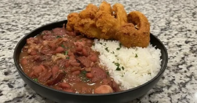 Plate of crispy chicken wings nestled on fluffy white rice alongside a bowl of red beans in a rustic setting.
