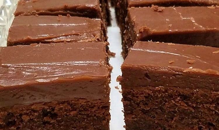 Close-up photo of warm, freshly baked chocolate fudge brownies with rich, crackly tops and gooey centers, cut into squares on a serving plate.