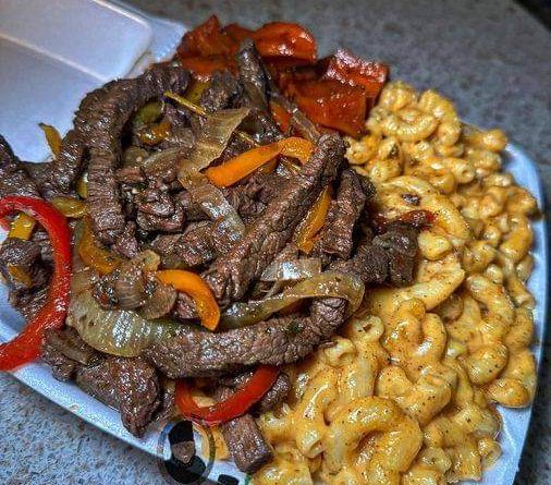 A photo of sizzling pepper steak pieces on a plate next to a bowl of creamy mac and cheese and roasted sweet potato wedges.