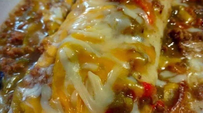 Wet burritos served on a plate with melted cheese, lettuce, and garnished with chopped green onions.