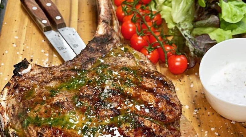 thick-cut Tomahawk steak seasoned with herbs and spices, sizzling on a hot grill with flames leaping up around it.