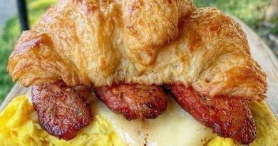 A golden brown croissant cut in half, filled with crispy bacon, fluffy scrambled eggs, and melted cheddar cheese.