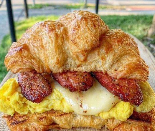A golden brown croissant cut in half, filled with crispy bacon, fluffy scrambled eggs, and melted cheddar cheese.