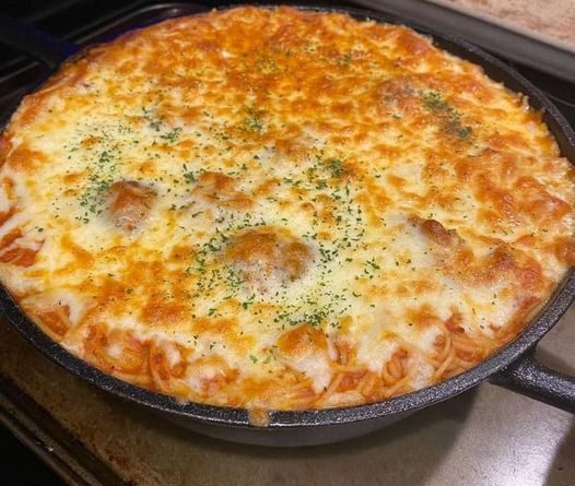 A bubbling casserole dish filled with baked spaghetti, overflowing with melted mozzarella cheese and flecks of fresh parsley.