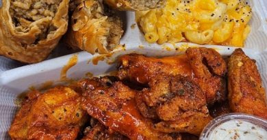 A platter piled high with Cajun dishes: Dirty Rice Boudin Egg Rolls (golden brown and crispy), Crack Mac and Cheese (creamy and bubbly), and Lemon Bae Wings (glazed and glistening).