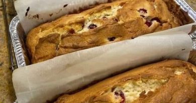 A close-up photo of a sliced Cream Cheese Cranberry Loaf on a plate. The loaf is golden brown on the outside and has swirls of cream cheese and bright red cranberries throughout.