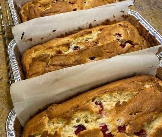 A close-up photo of a sliced Cream Cheese Cranberry Loaf on a plate. The loaf is golden brown on the outside and has swirls of cream cheese and bright red cranberries throughout.