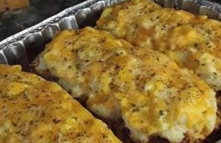 A close-up of a meatloaf on a plate, topped with melted cheese and served with mashed potatoes.