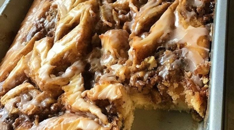 A close-up photo of a sliced Cinnabon Cinnamon Roll Cake revealing a gooey cinnamon swirl center and a creamy white glaze drizzled on top.