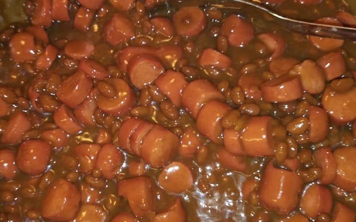 A baking dish filled with juicy hot dogs, baked beans, and a sweet and savory sauce.