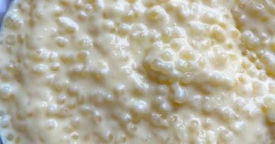 A close-up view of a glass bowl filled with homemade tapioca pudding. The pudding is topped with whipped cream and a maraschino cherry.