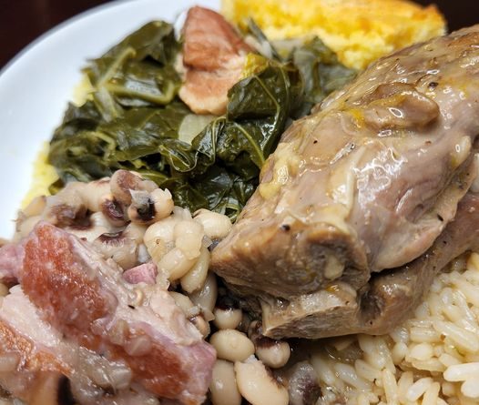 A plate filled with mixed greens, smothered turkey necks, blackeye peas, rice, and cornbread, showcasing a traditional Southern meal.