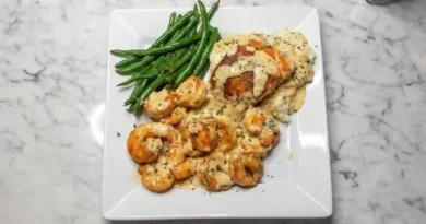 Close-up of a plate with Cajun-spiced shrimp and salmon drizzled in a rich, golden garlic cream sauce. Creamy mashed potatoes and vibrant green beans are arranged alongside.
